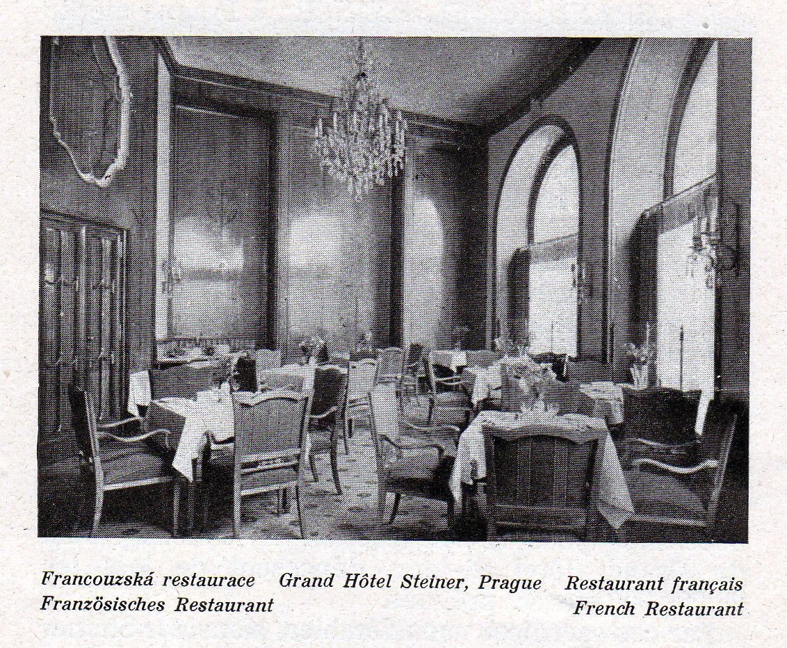 Vintage black-and-white hotel dining room with set tables, chairs, tall arched windows, and a chandelier