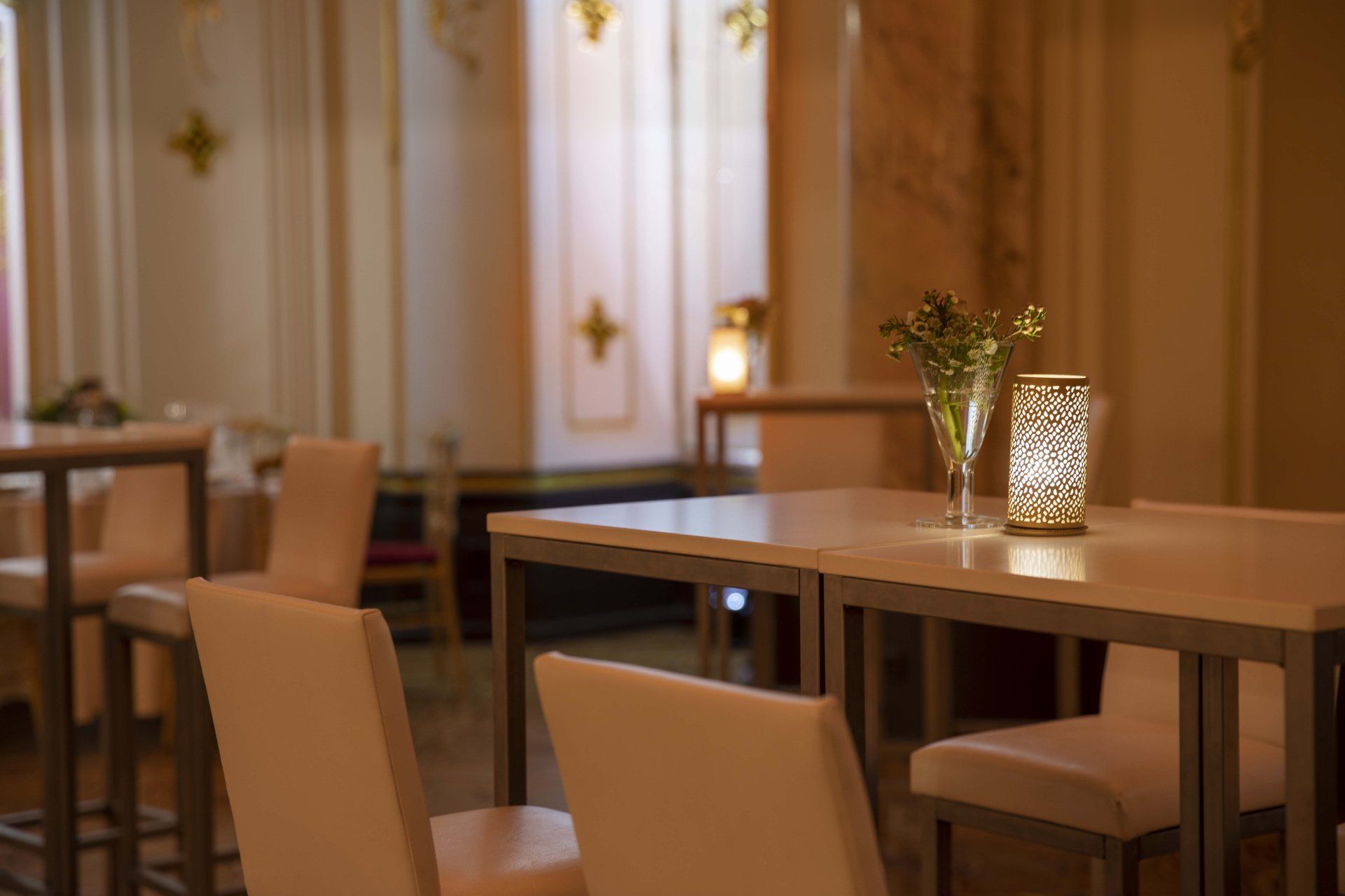 Empty restaurant dining area with beige chairs, wooden tables, and warm ambient lighting