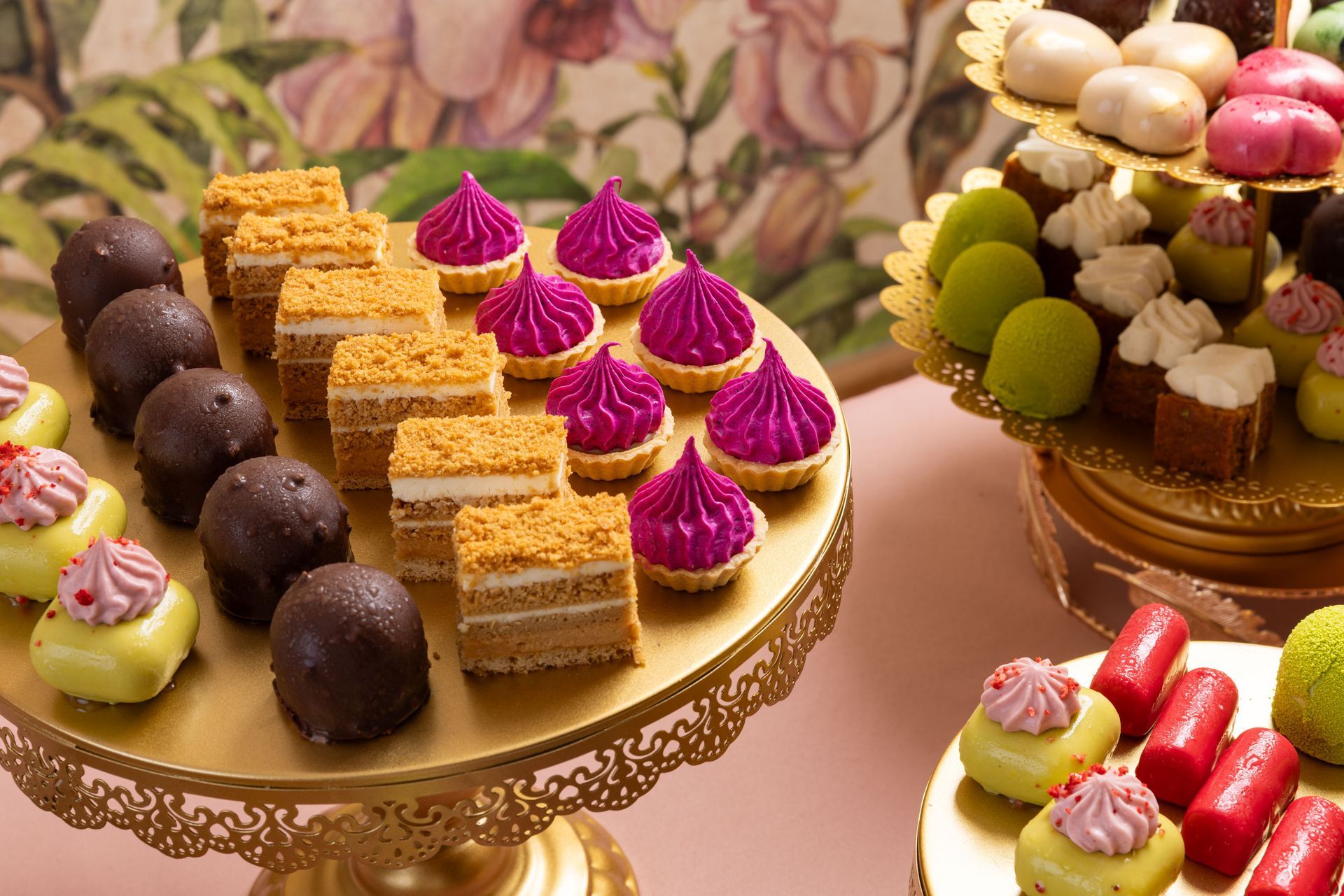 Různé barevné petit fours a cukrovinky na zlatých podnosech na dezertní displeji