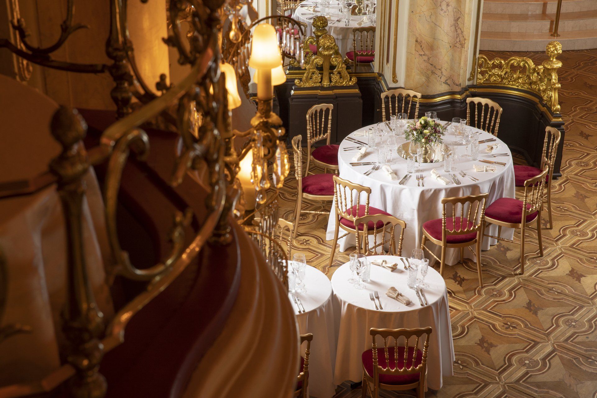 Elegant banquet hall with round tables, red chairs, and gold decor viewed from a staircase