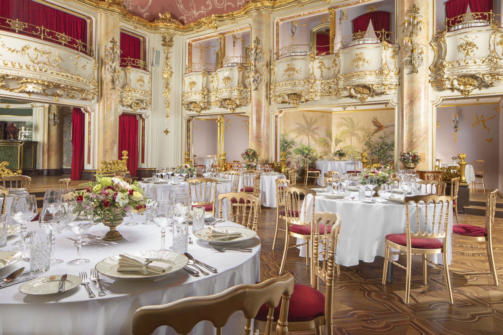 Elegant banquet hall with gold decor, red curtains, and round tables set for a formal event