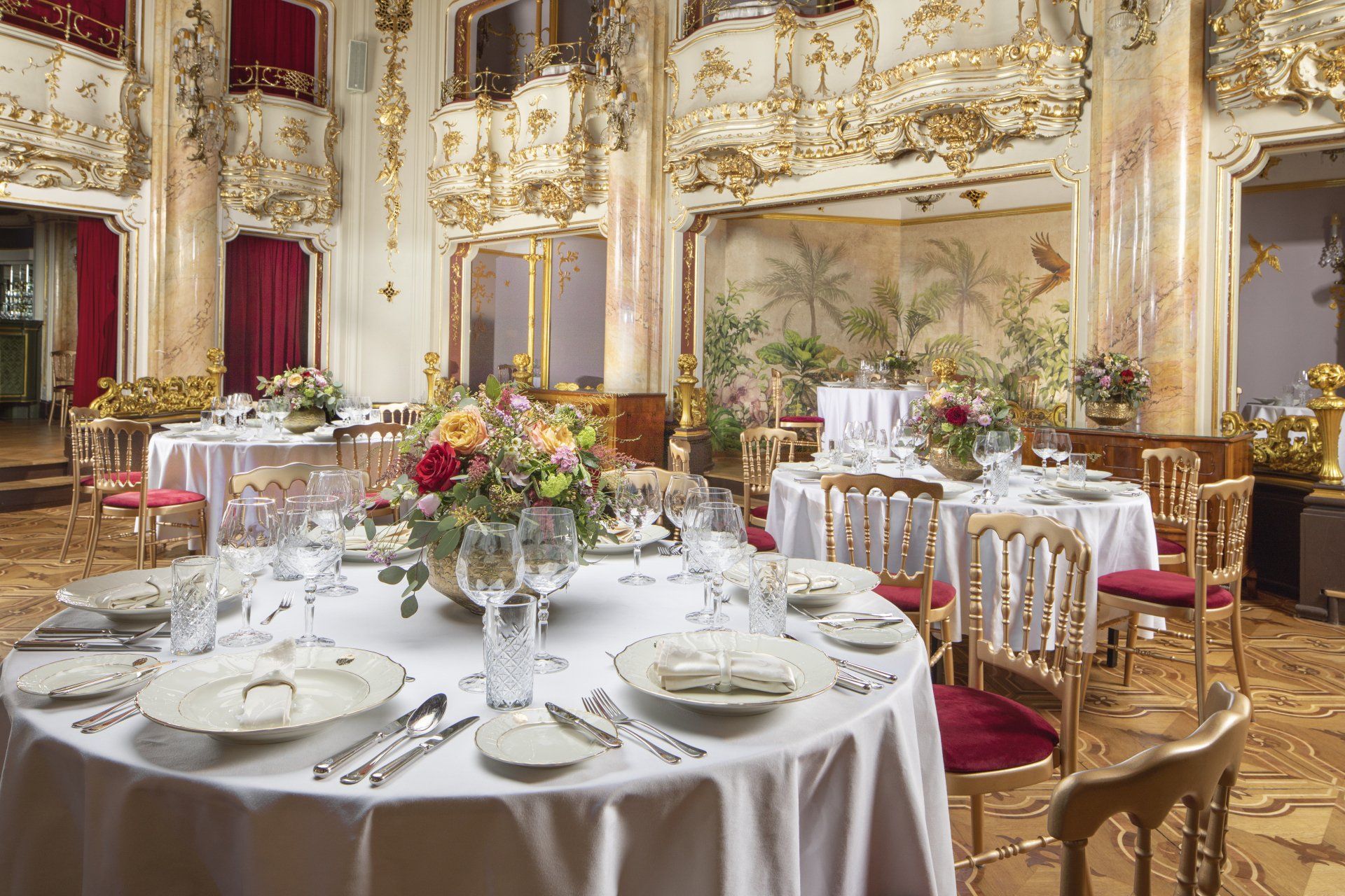 Elegant banquet table set in a gilded ballroom with white linens, flowers, and gold chairs