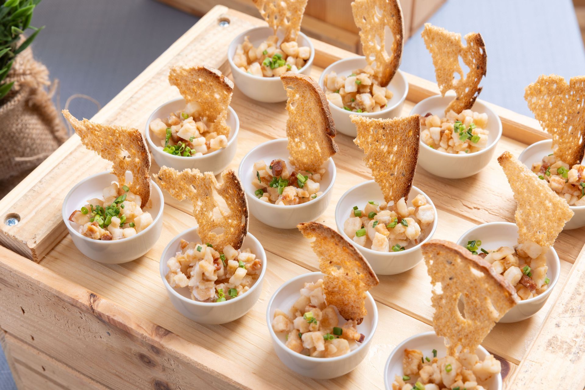 Small appetizer cups with diced salad and toasted bread crisps on a wooden serving tray.