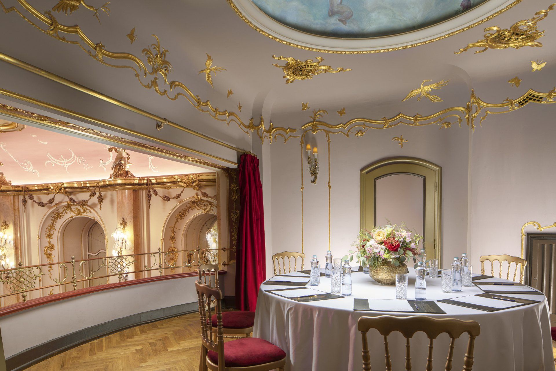 Elegant dining room with round table, white linens, gold trim, and a balcony view