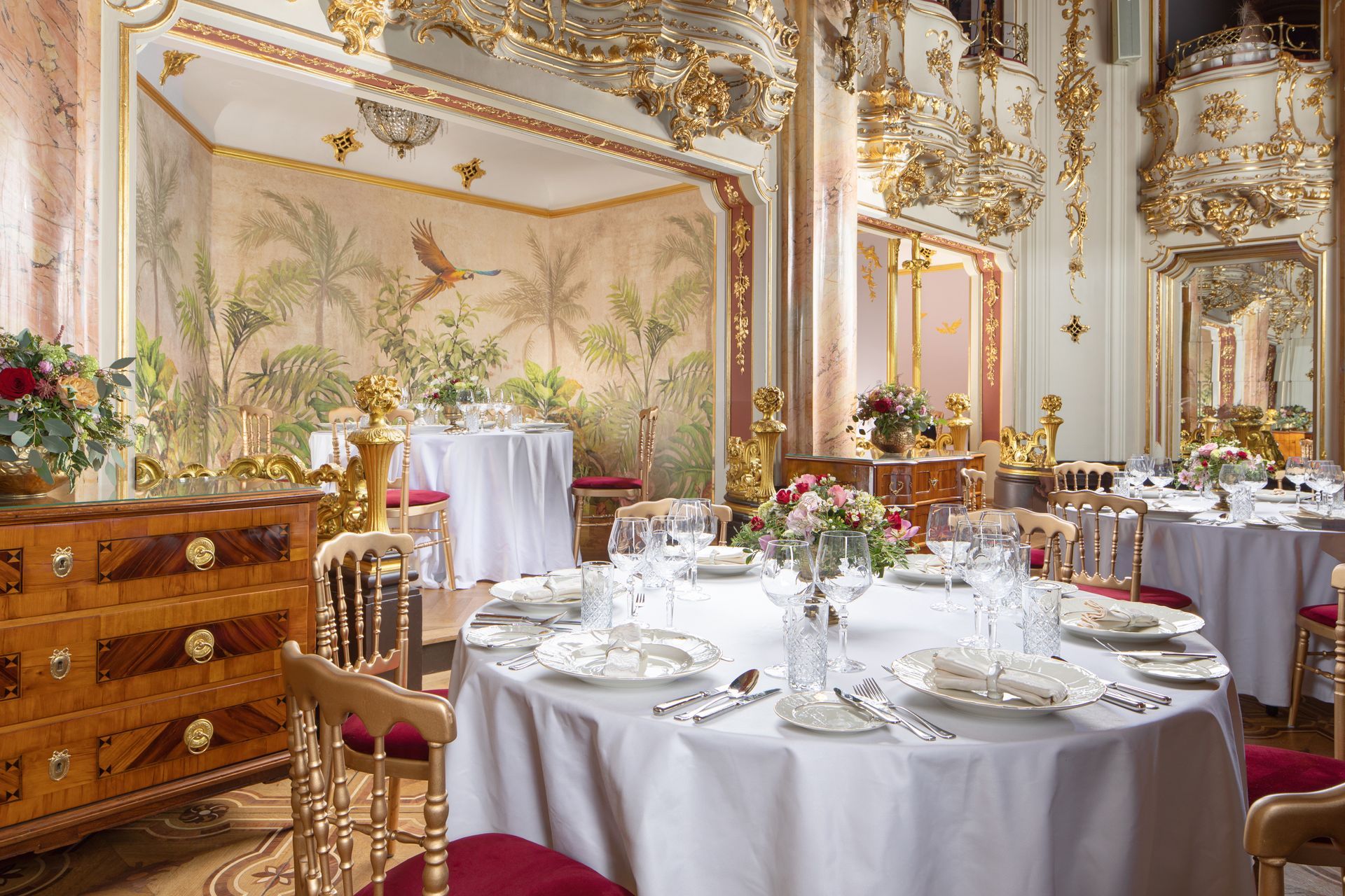 Elegant banquet room with round white-clothed tables, gold mirrors, and ornate decor