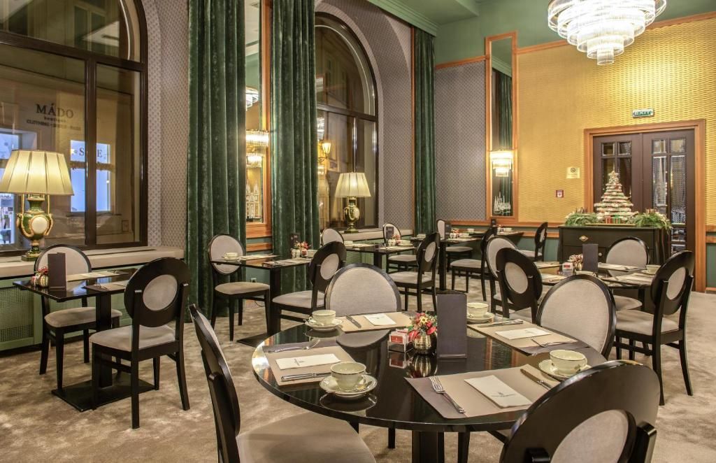 Elegantní hotelová jídelna s prostřenými stoly, lustry, zelenými závěsy a teplým osvětlením