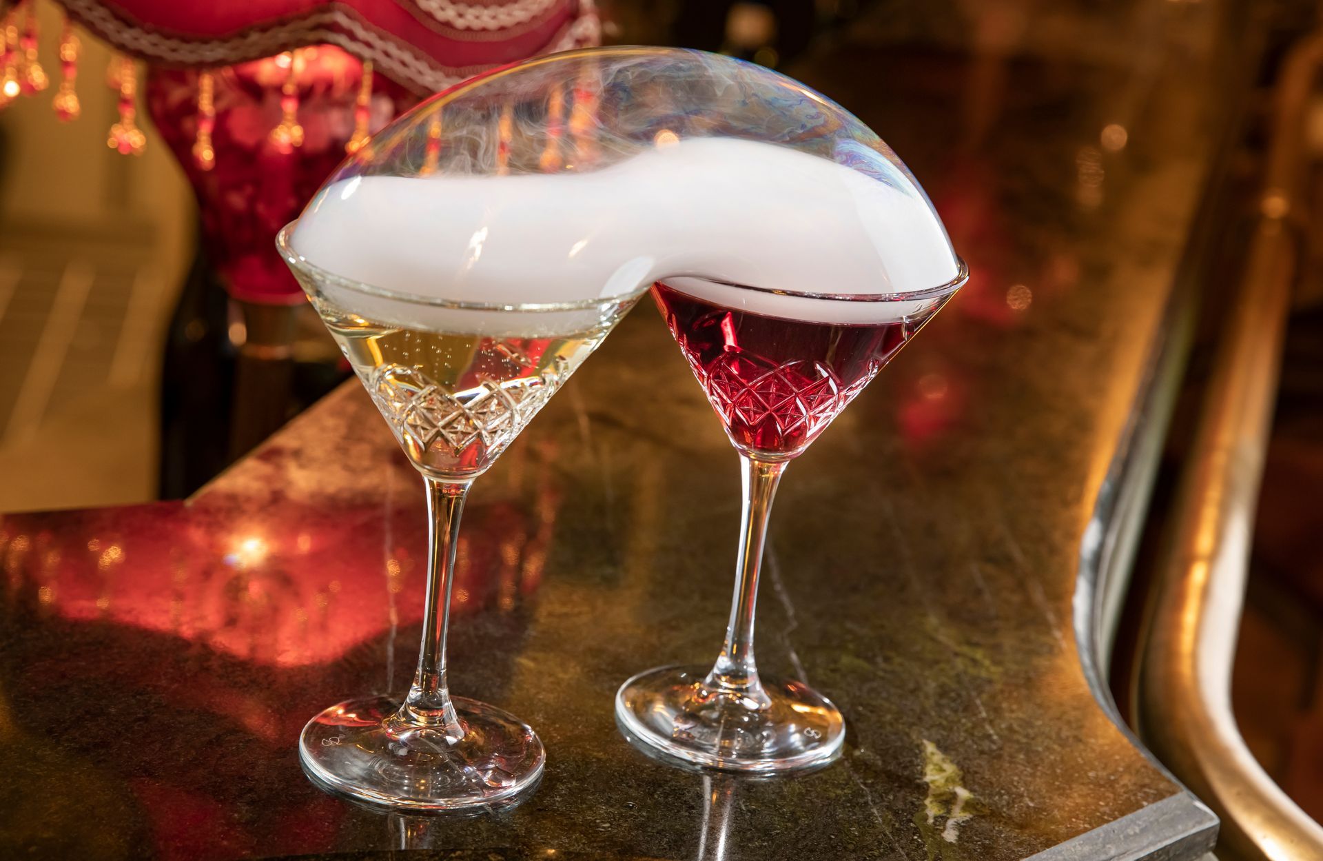 Dvě sklenice na martini s bílým a červeným pěnivým nápojem na barovém pultu