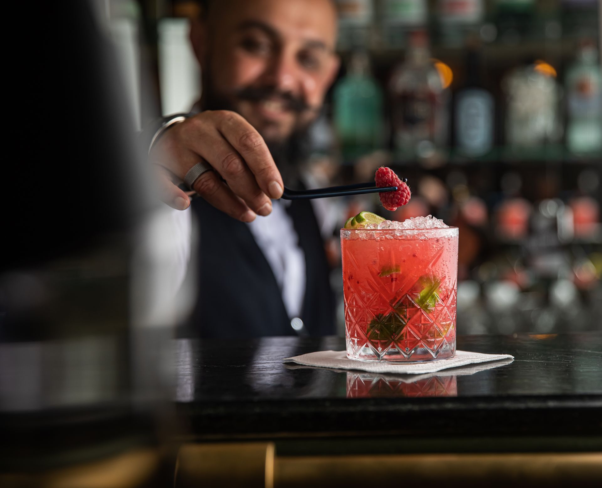Barman zdobí růžový koktejl malinou v baru.