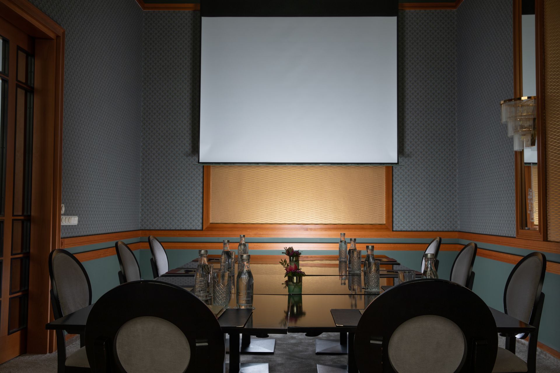 Empty conference room with a large projection screen and a long table surrounded by chairs.