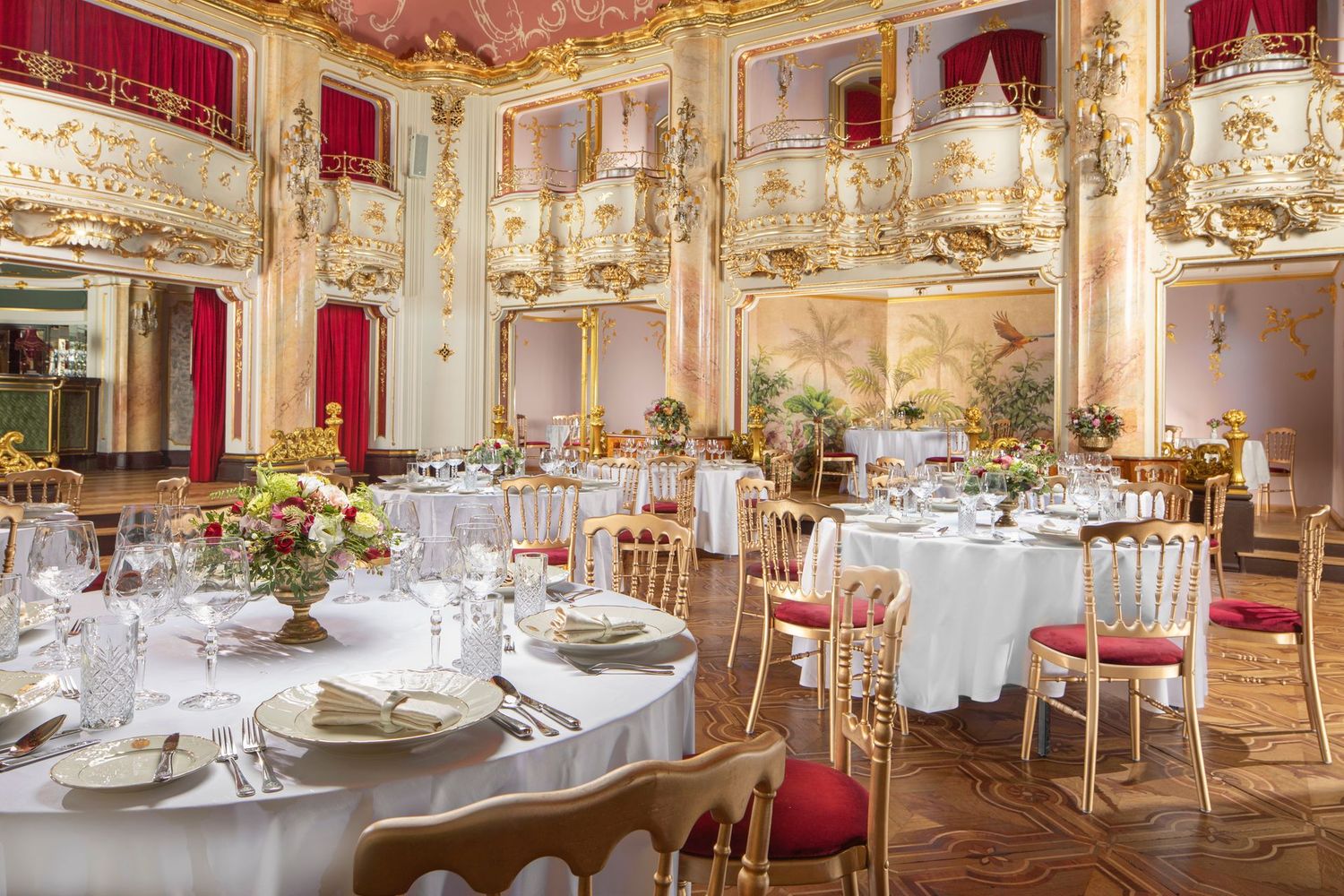 Elegant banquet hall with round tables set for a formal event, crystal chandeliers, gold trim, and red drapes
