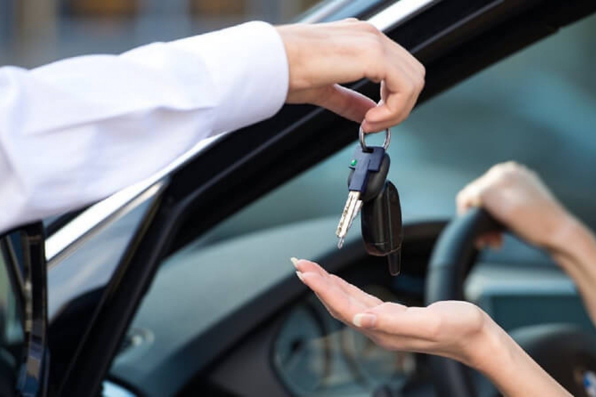 Handing over car keys between two people beside an open vehicle door