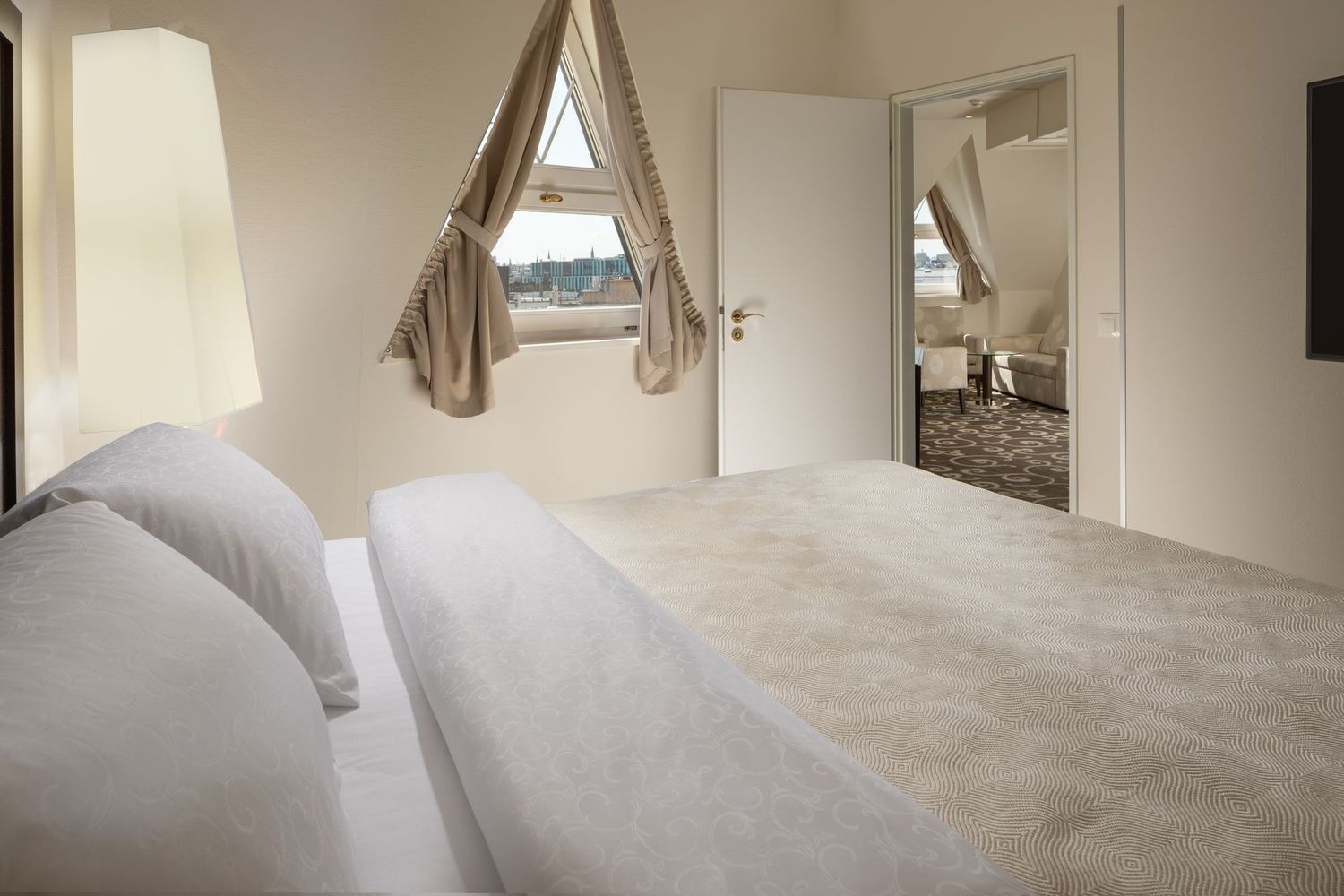 Bright bedroom with a white bed, beige walls, window, and mirrored closet door