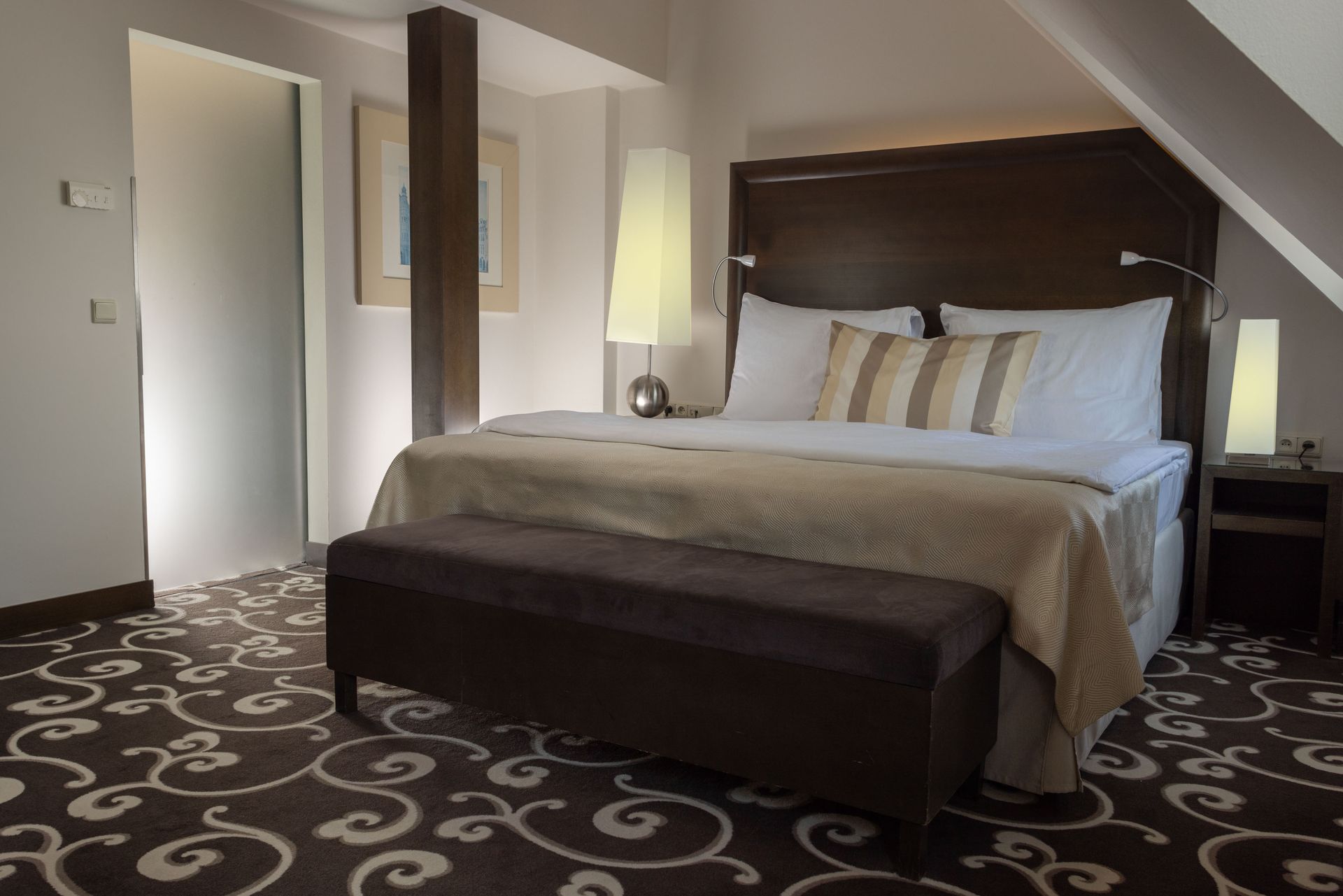 Modern hotel room with a large bed, dark carpet, and soft bedside lighting