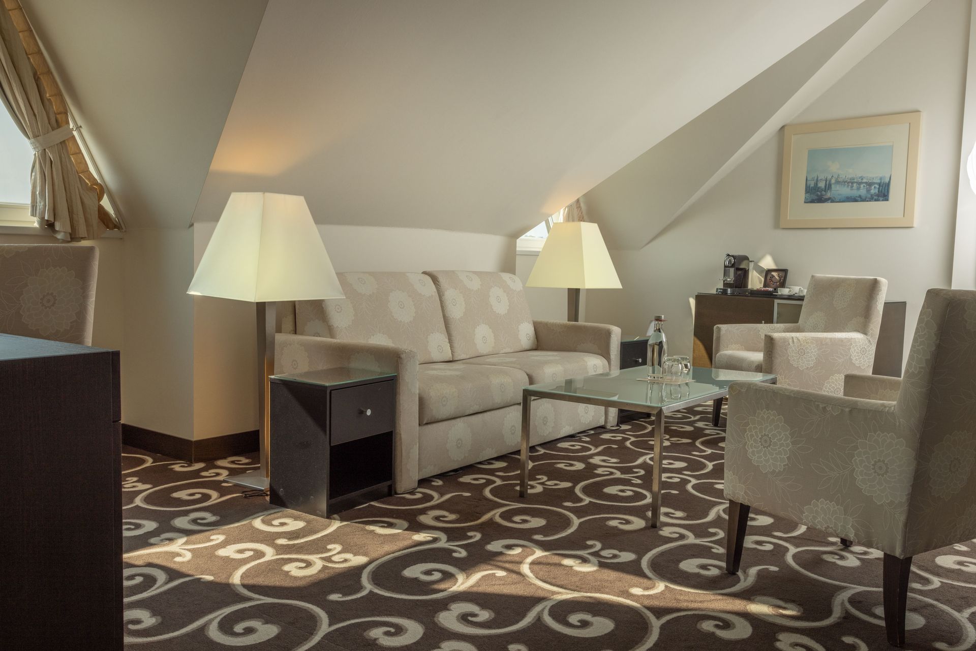 Cozy attic living room with sofa, armchairs, glass table, lamps, and patterned carpet