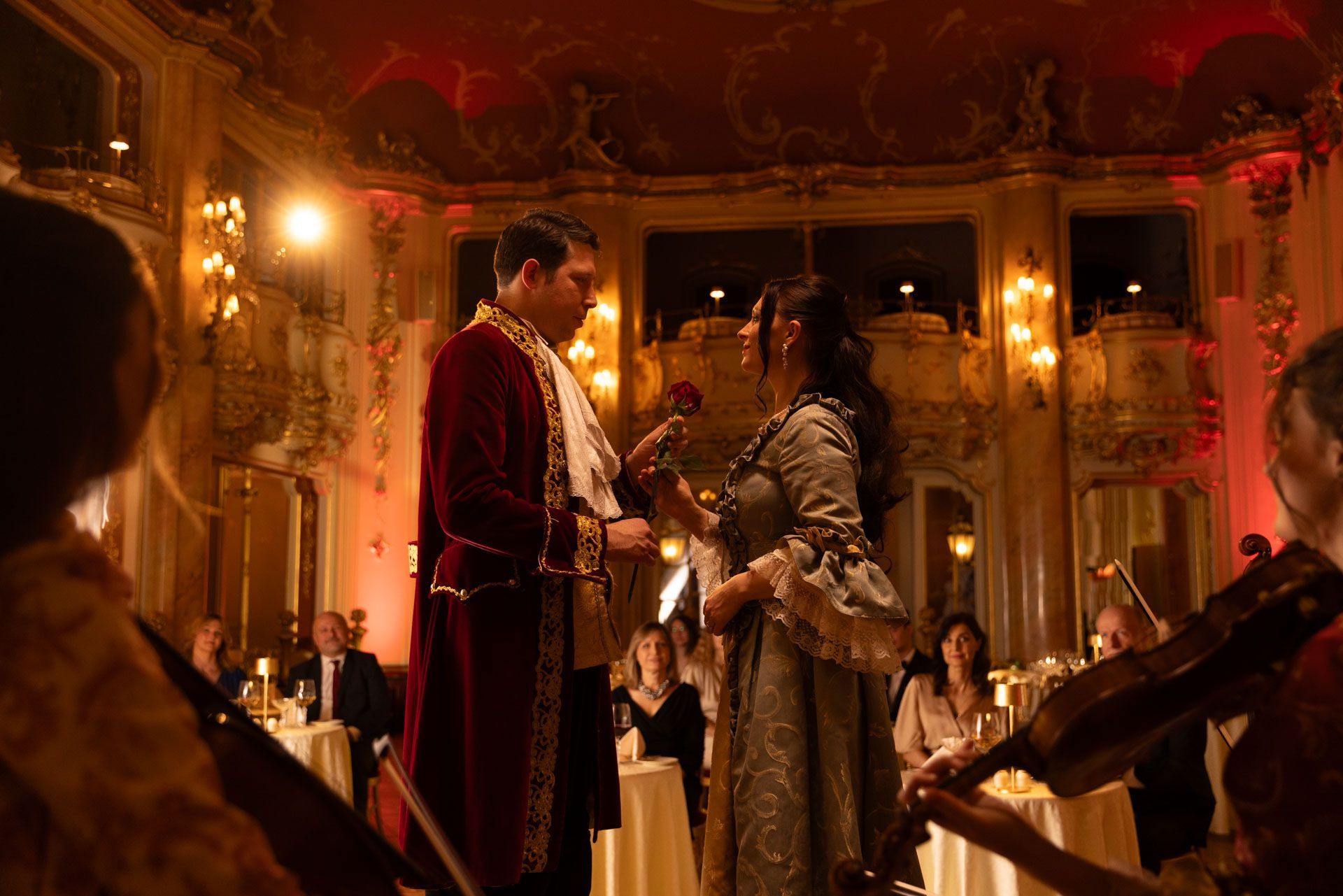 Elegant ballroom scene with a couple in ornate historical costumes under warm candlelight