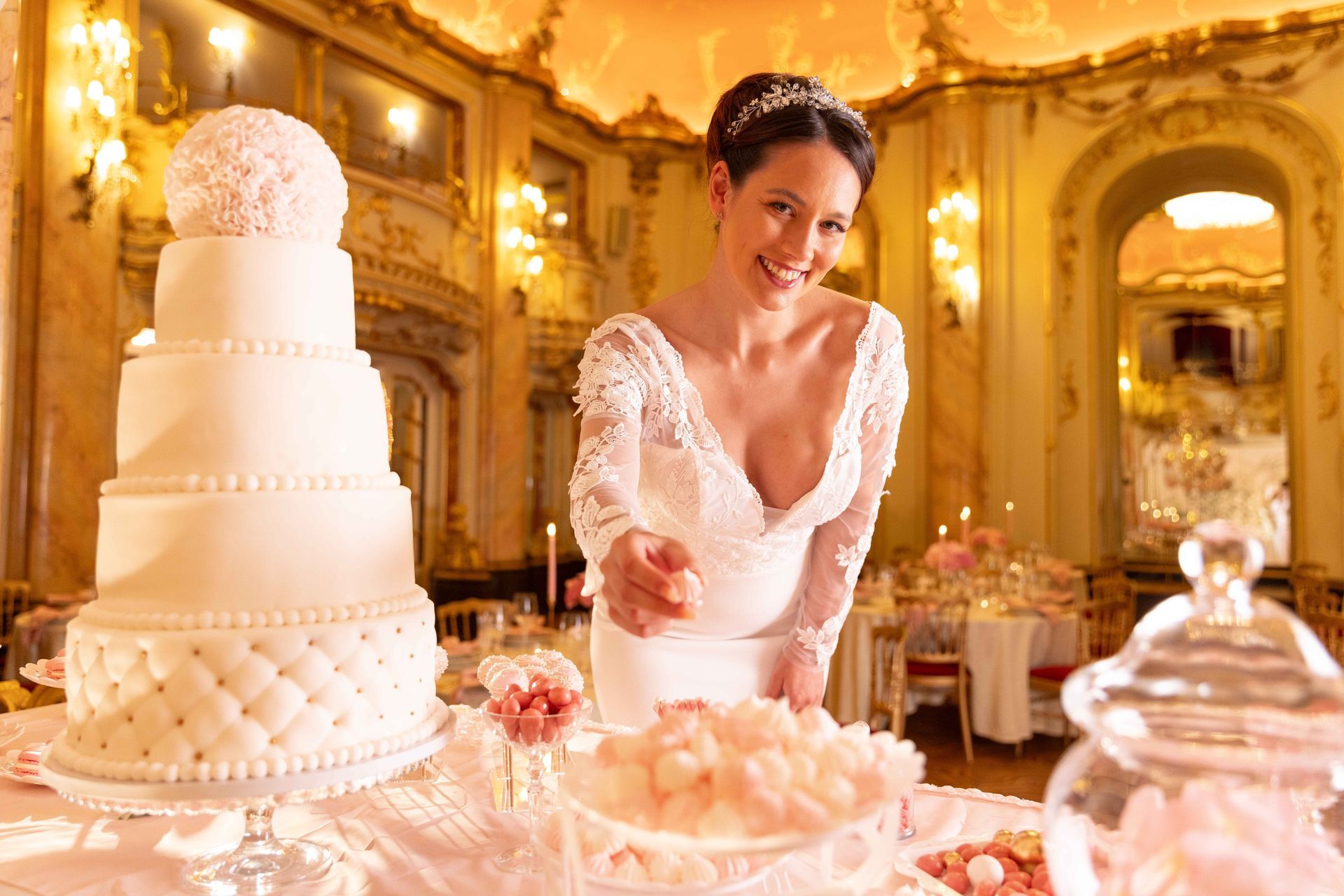 Woman serving cake beside a tall white wedding cake in an elegant golden banquet hall
