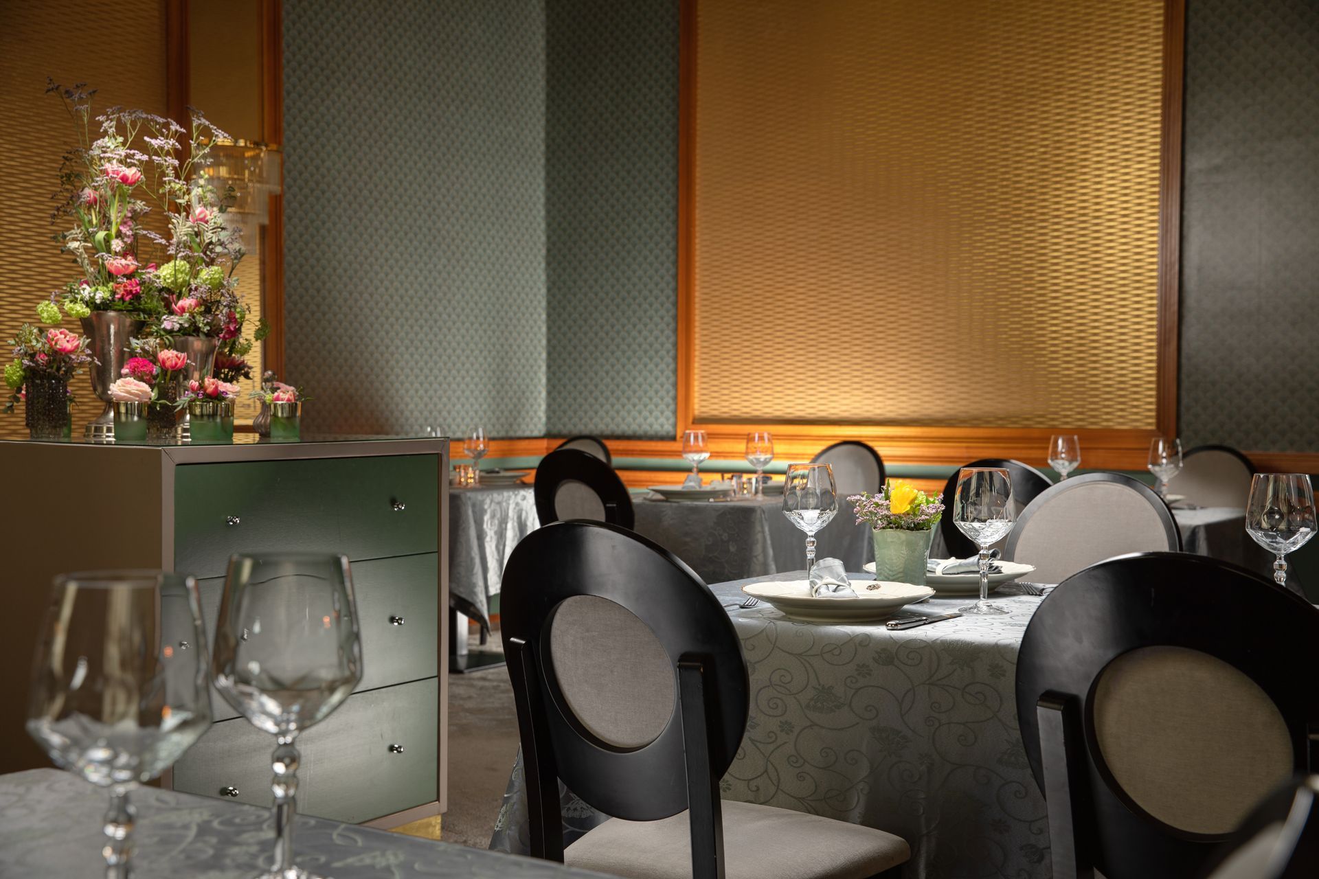 Elegant restaurant dining room with set tables, black chairs, wine glasses, and a flower arrangement
