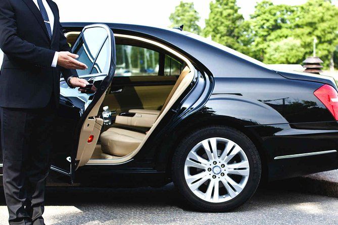 Man opening the rear door of a black sedan in a driveway or parking lot