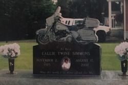 Motorcycle on a black grave marker with floral urns on both sides in a cemetery plot