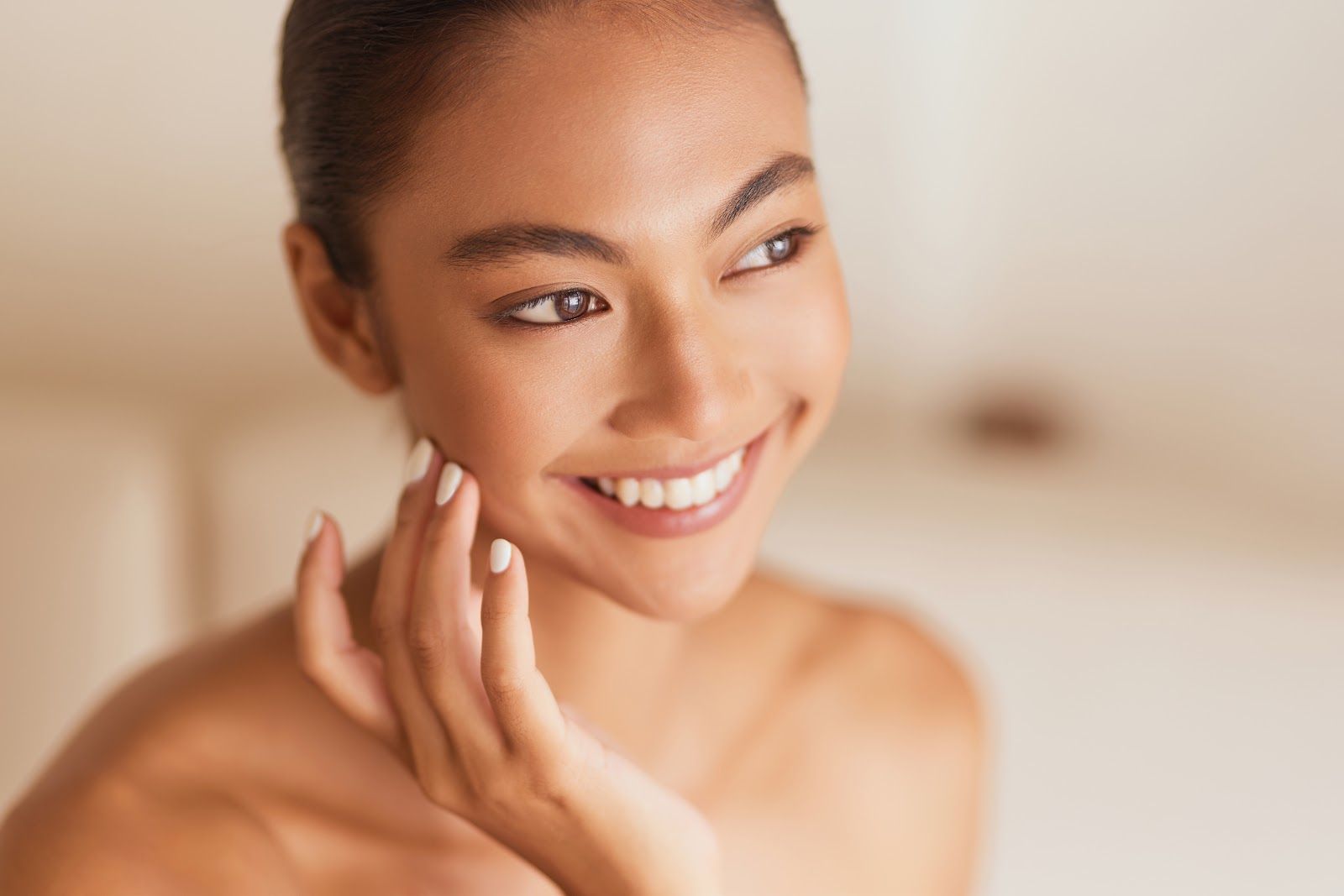 Smiling woman applying cream to her cheek in a softly lit close-up