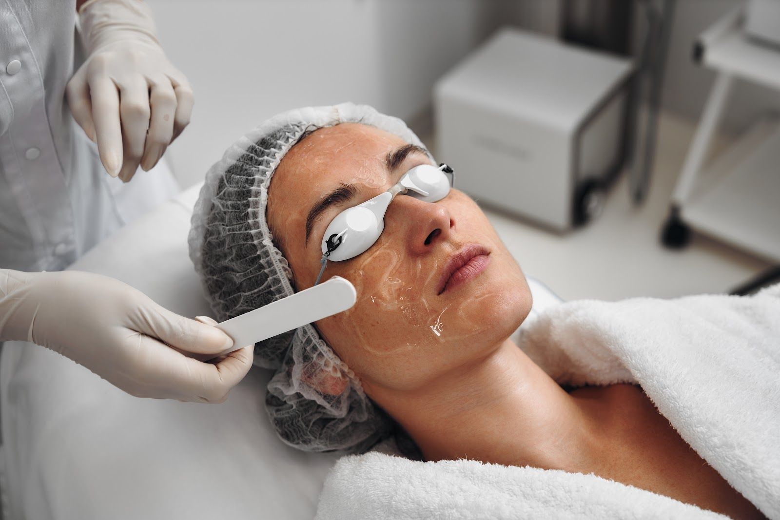 Facial treatment in progress, with a cream being applied to a reclining client wearing eye pads.