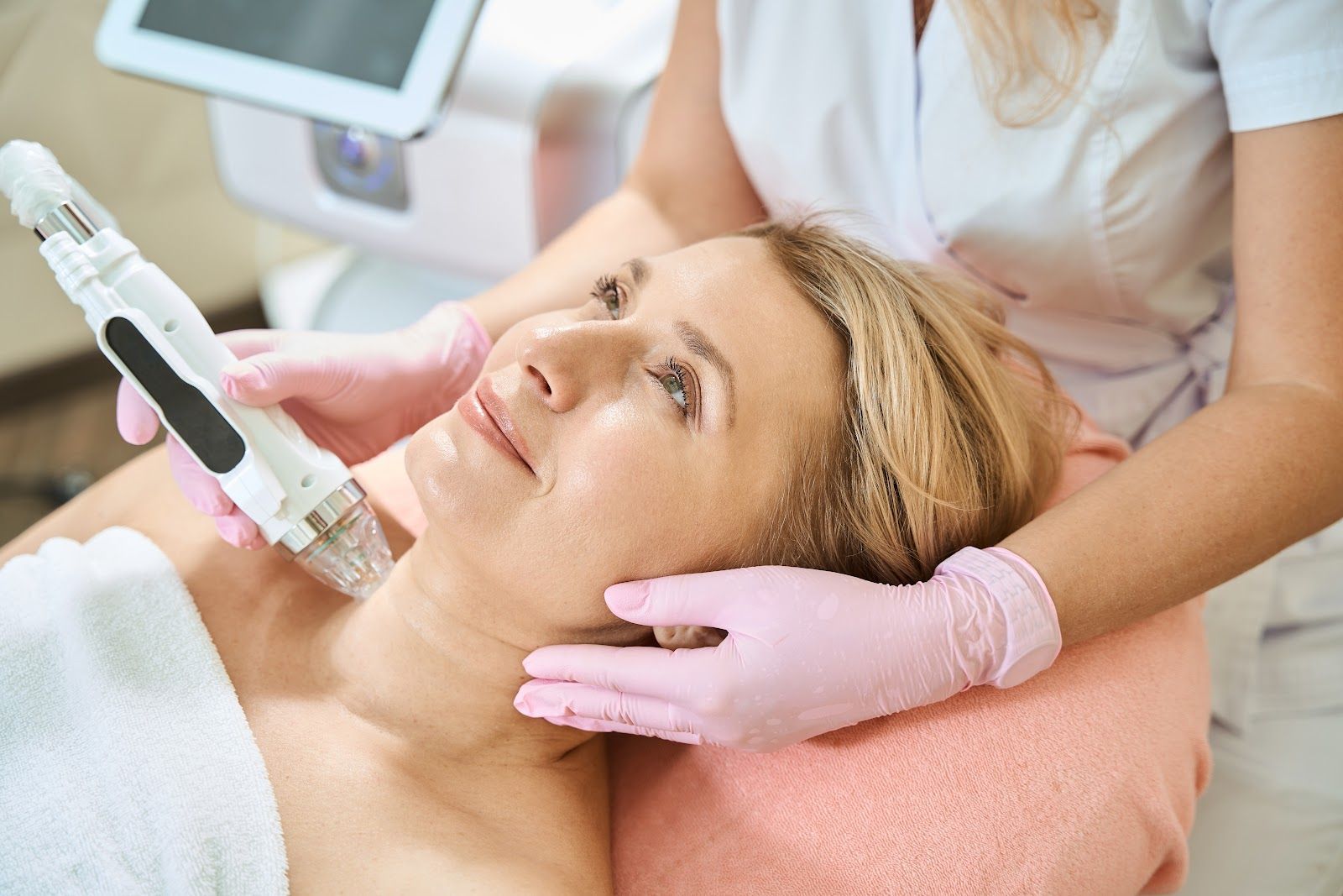 Cosmetic treatment with a handheld device on a woman lying on a pink treatment bed