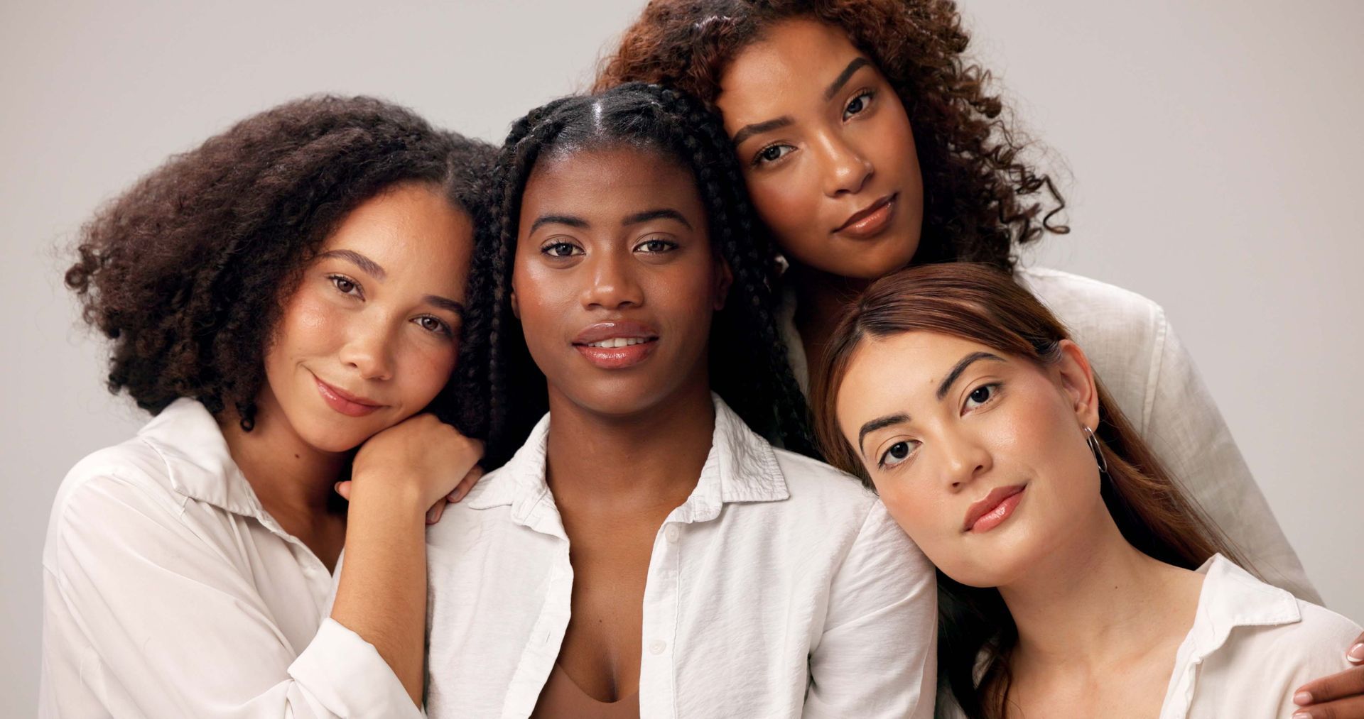 Four people in white shirts posing closely together against a light background, smiling softly.