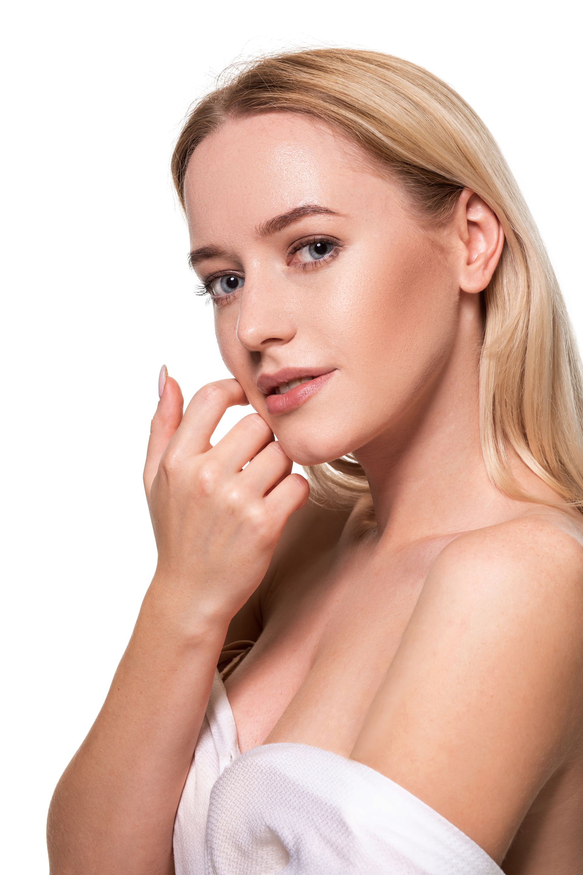 Blonde woman in a white towel posing against a white background, touching her face gently.