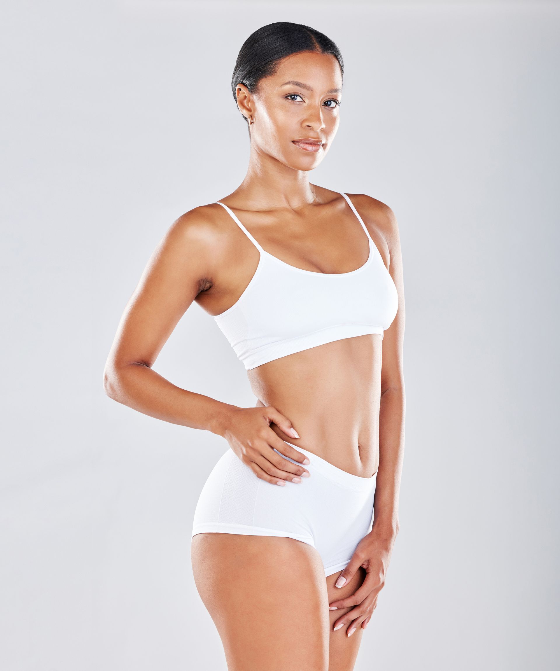 Woman in white sports bra and shorts standing against a light gray background.