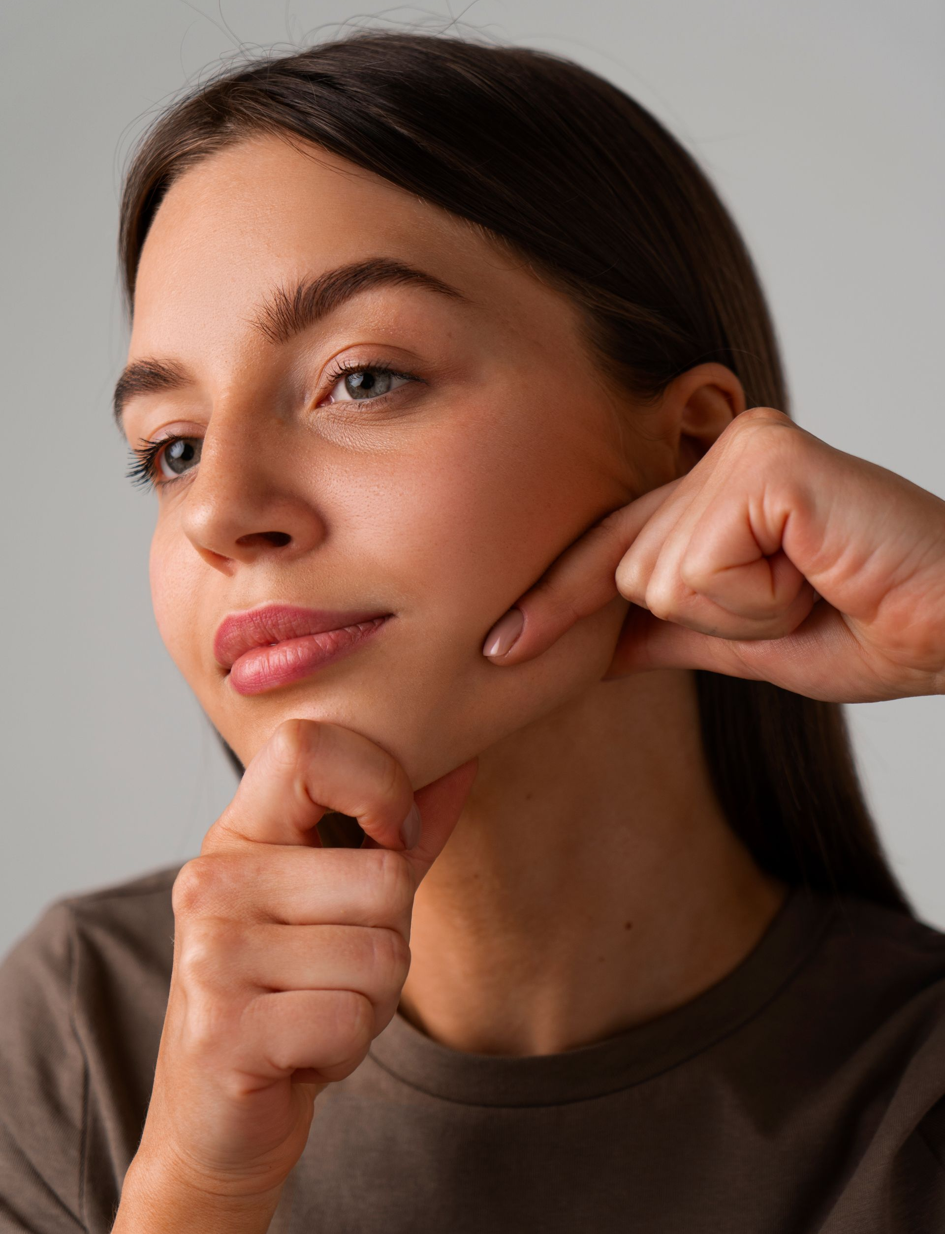 Person demonstrating a facial massage on their cheek and jawline against a plain background