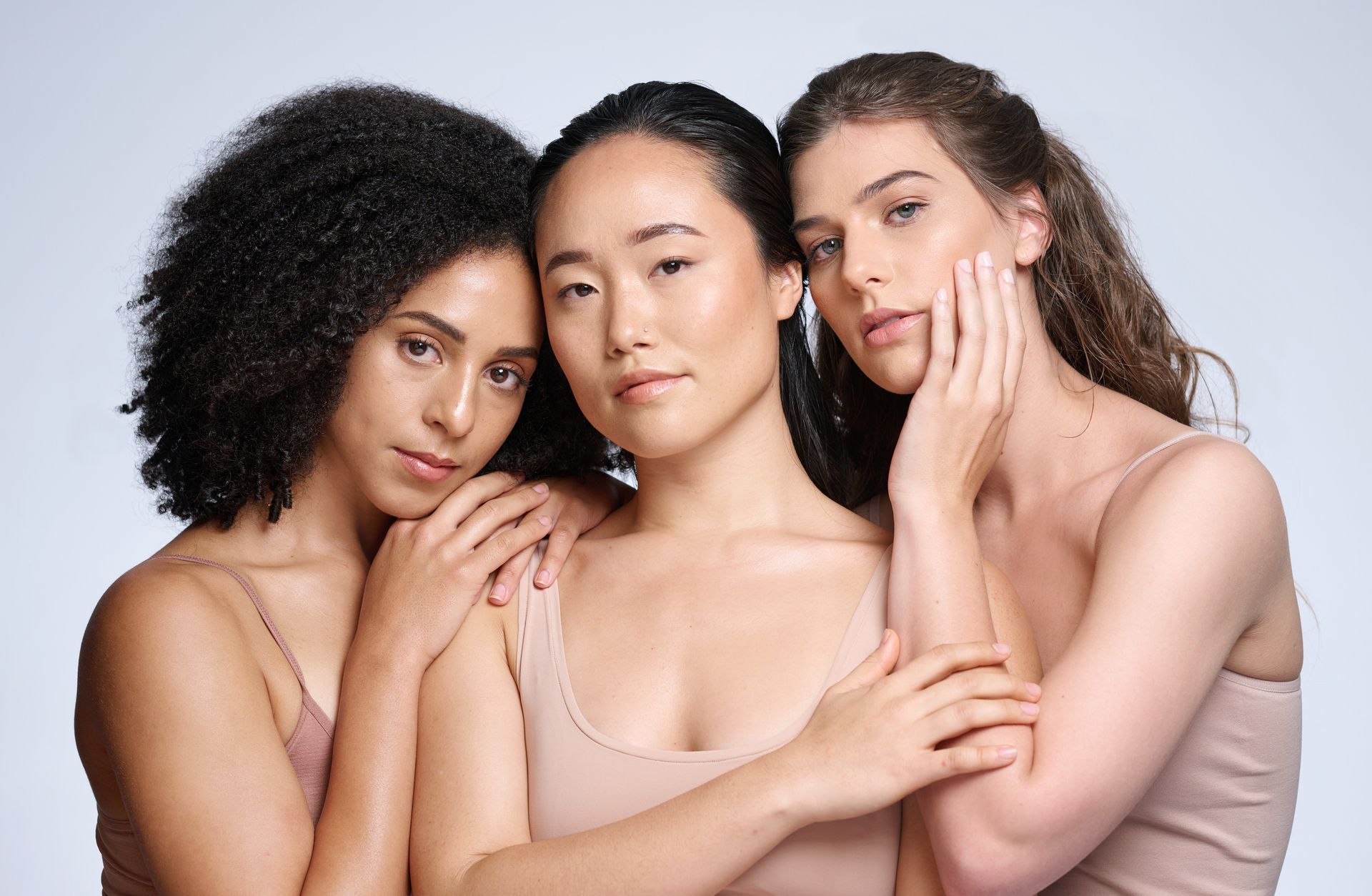 Three people posing closely together against a light background, wearing neutral-toned tops.
