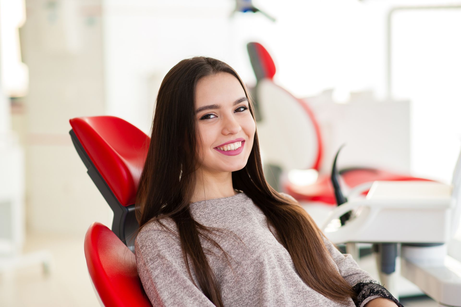 Woman smiling in a red dental chair inside a bright clinic