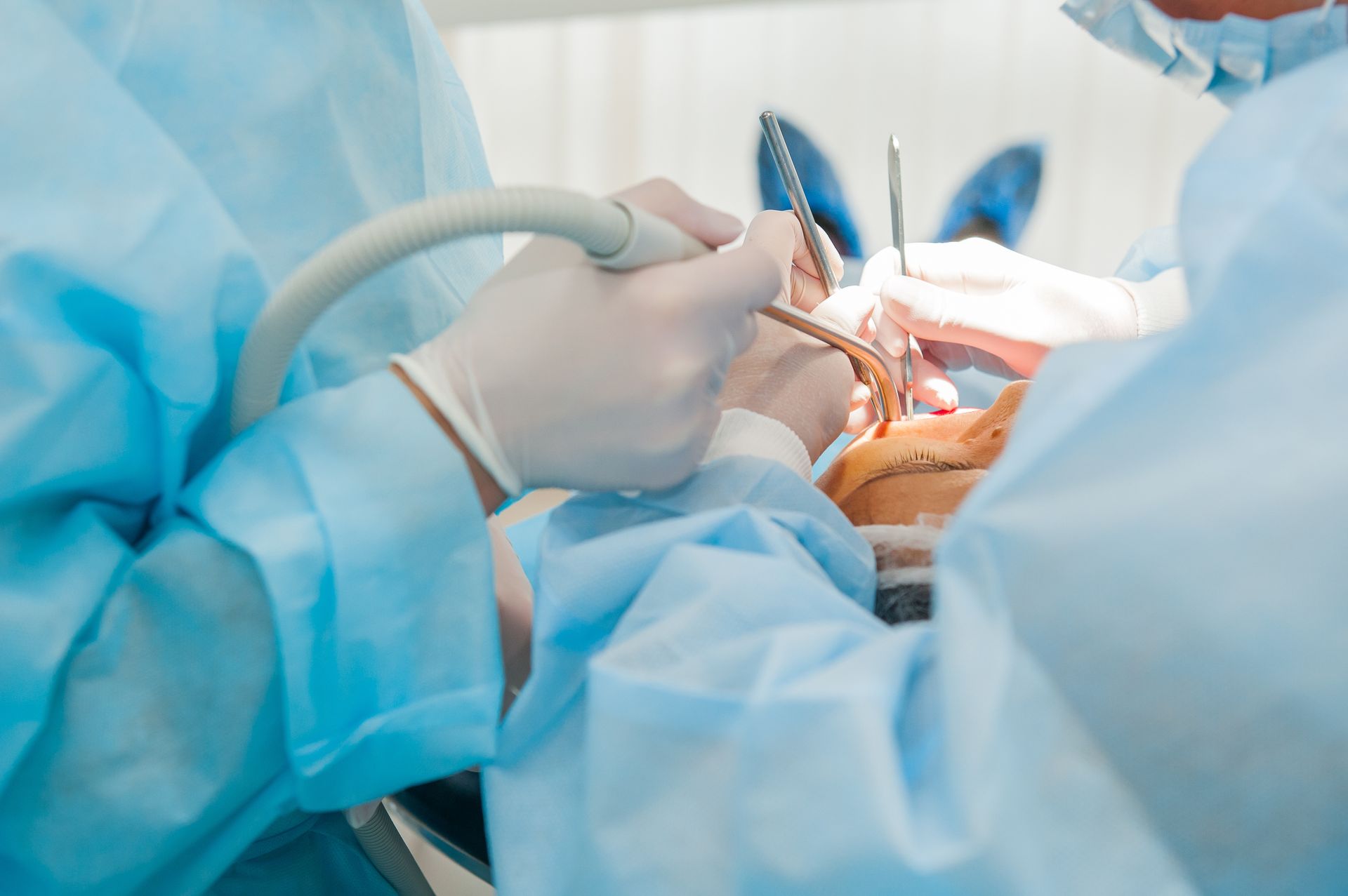 Surgeons in blue scrubs performing an operation with surgical tools and bright operating lights