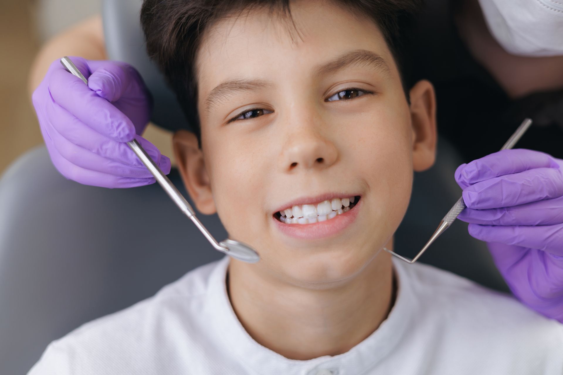 Dentist cleaning a smiling patient’s teeth with purple-gloved hands