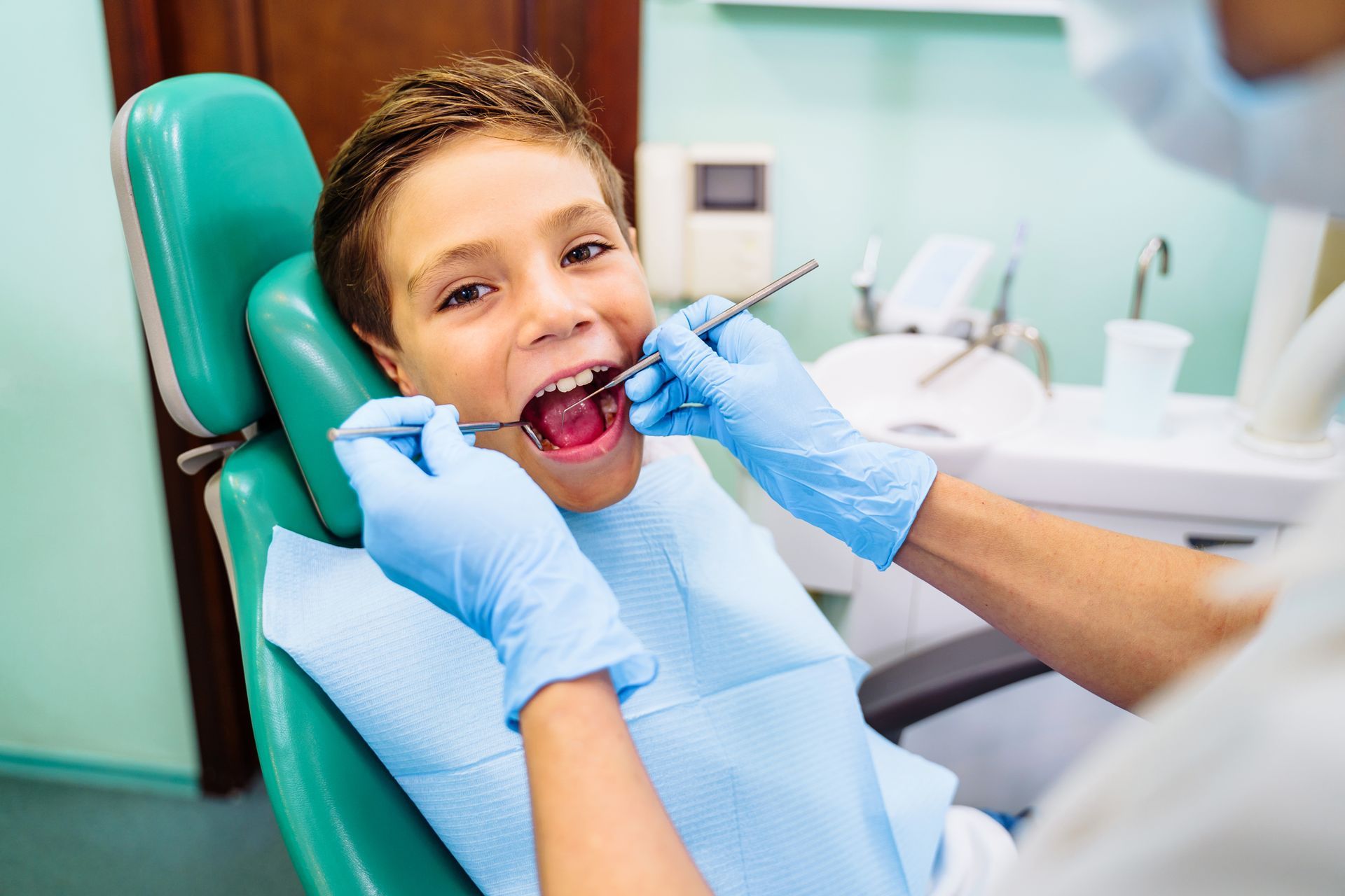 Child in a dental chair while a dentist examines their mouth with gloved hands.