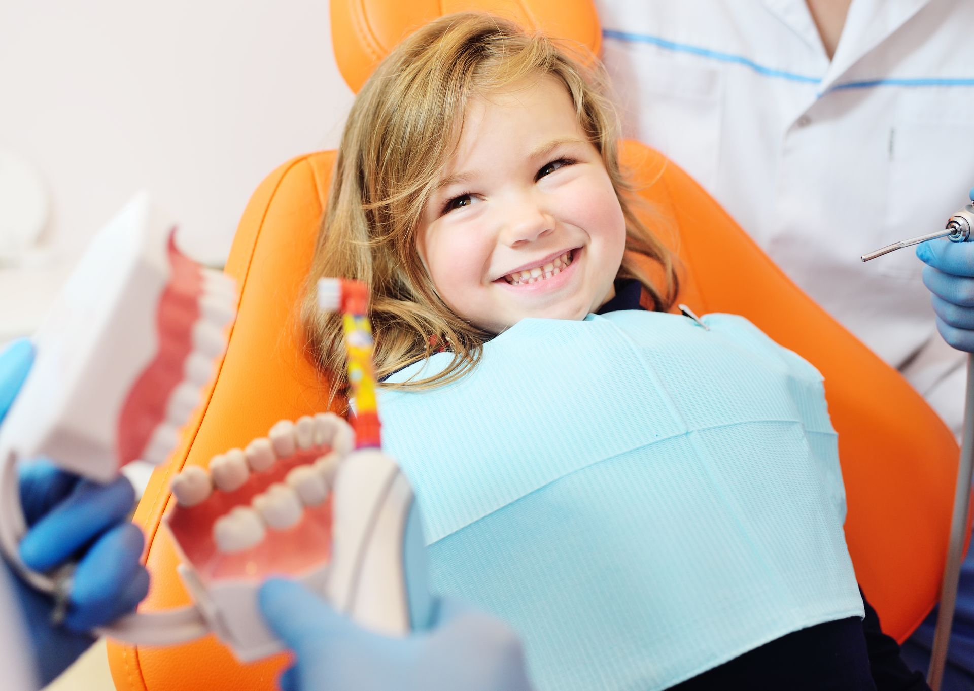 Smiling child in a dental chair during a dental exam, with tools and a dentist nearby
