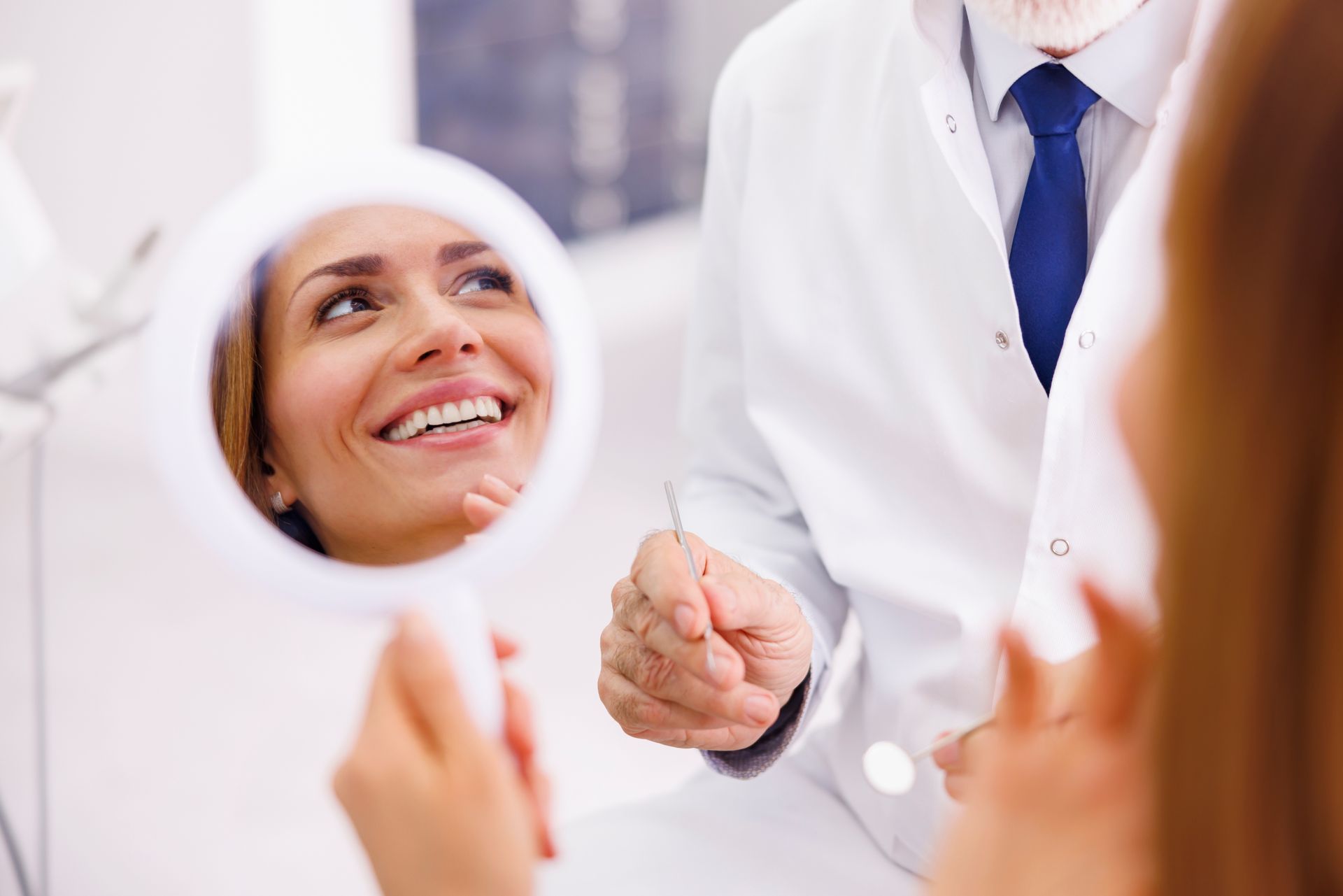 Dentist holding a mirror for a smiling patient in a bright clinic