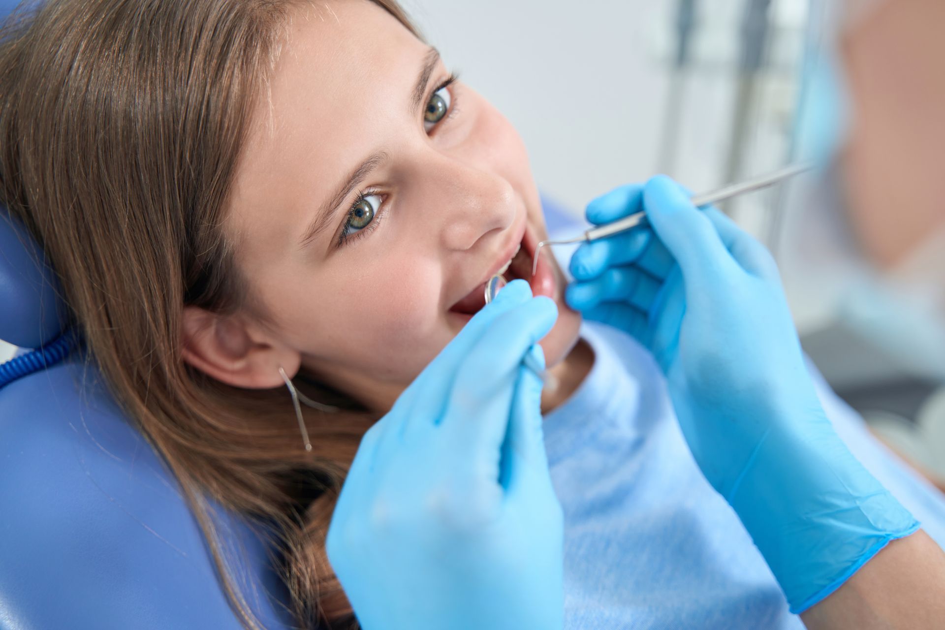 Patient at dentist as gloved hands examine her teeth with dental tools