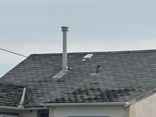 Gray shingled rooftop with a metal vent pipe and a skylight under a cloudy sky