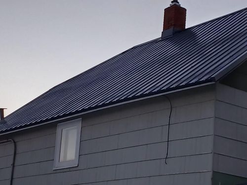 Gray house with a dark metal roof and chimney at dusk