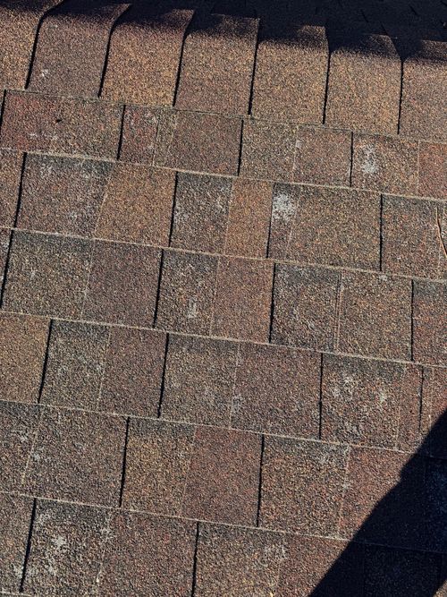 Close-up of brown asphalt roof shingles with a dark triangular shadow in the corner