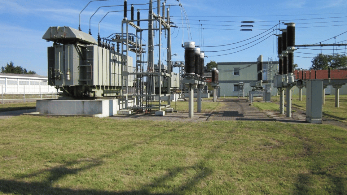 Electrical substation with transformers, insulators, and power lines on a grassy field under a blue sky.