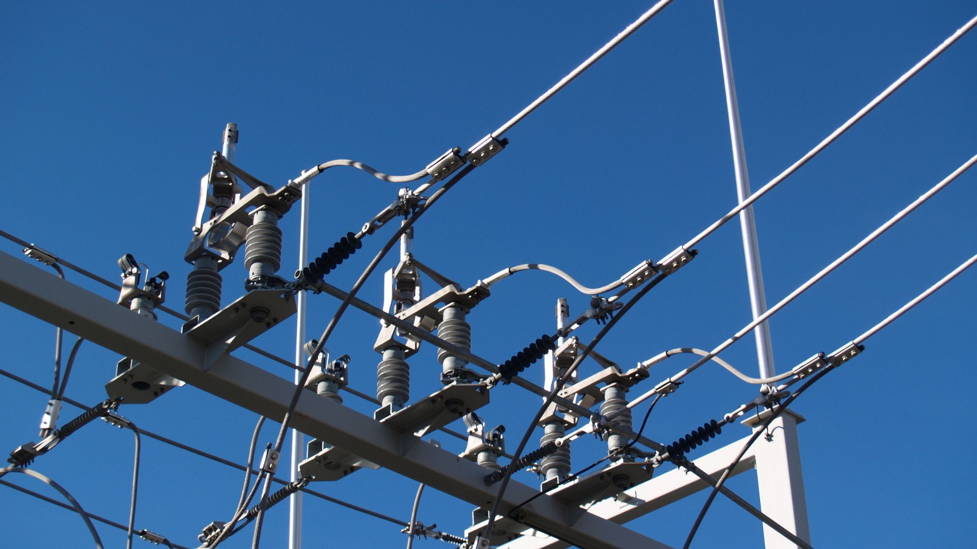High-voltage power lines and insulators against a clear, blue sky.