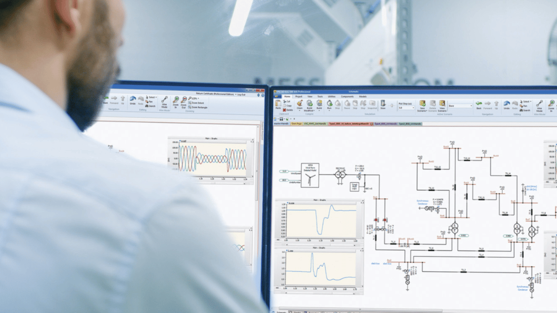 A person wearing a light blue shirt works at two computer monitors displaying complex engineering schematics and graphs.