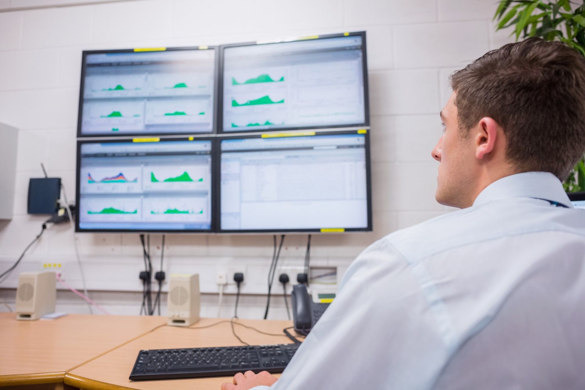 Man looking at four computer screens displaying graphs in a control room.