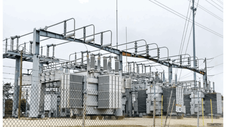 An electrical substation with several large transformers and metal support structures under an overcast sky.