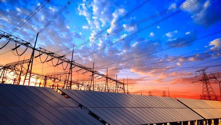Solar panels and power lines against a colorful sunset sky.