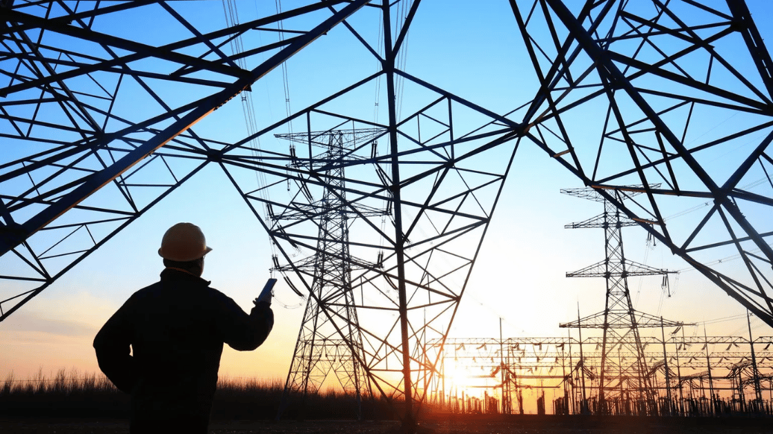 Engineer in silhouette inspecting electrical power grid at sunset.