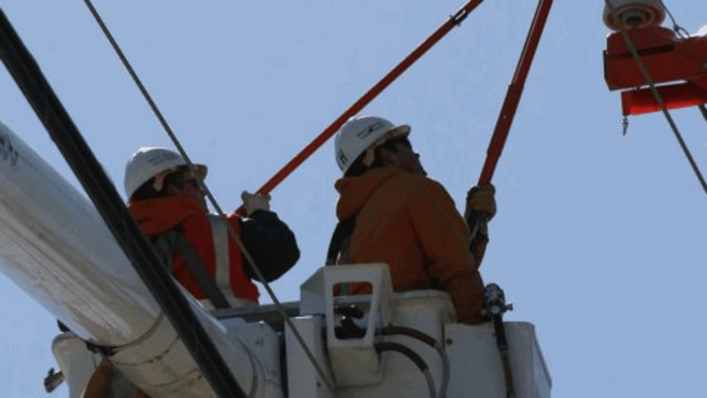 Two utility workers in bucket truck with tools working on power lines.