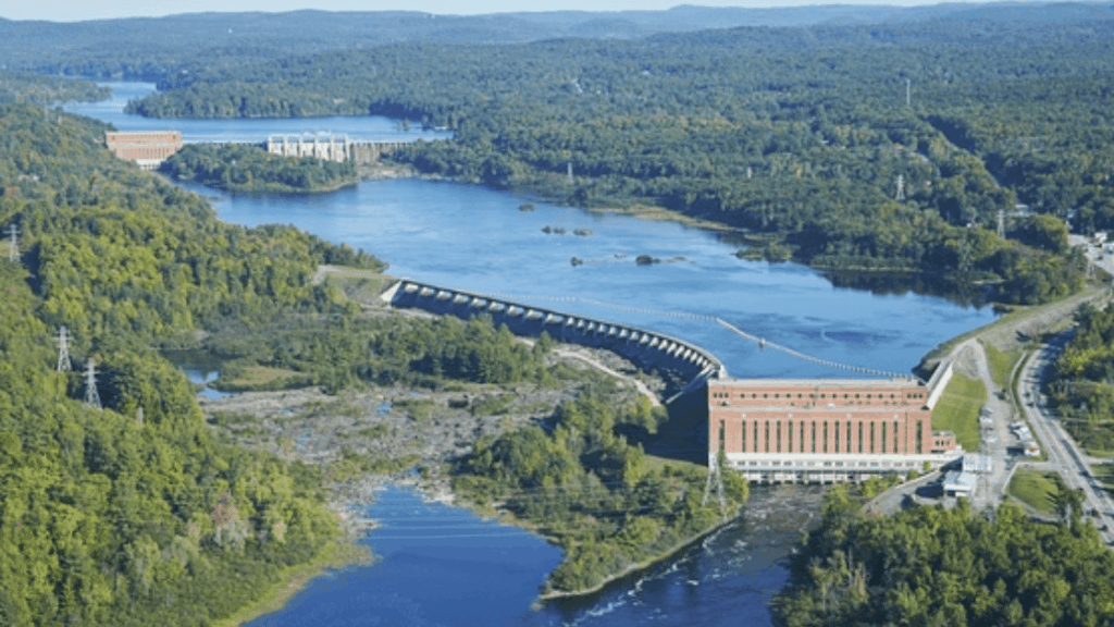 Hydroelectric dam complex on a river, surrounded by lush green forest.
